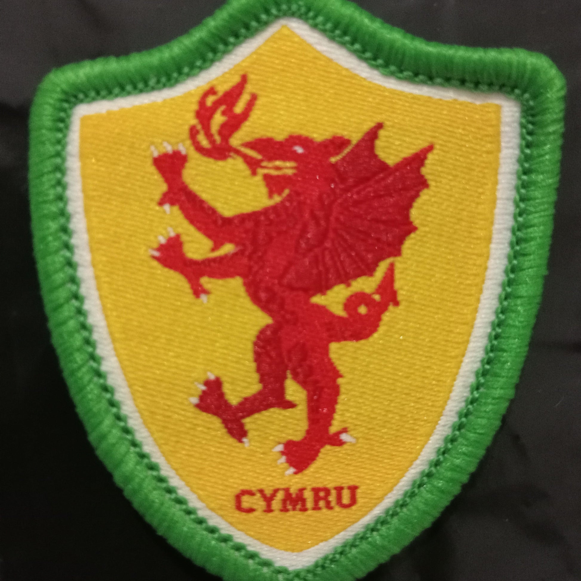 Embroidered patch with a red dragon on a yellow shield with green border, featuring the word 'Cymru'.
